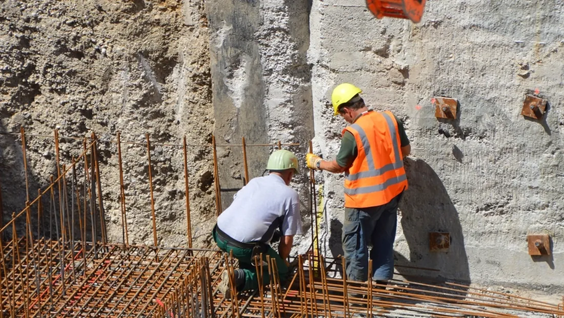 Due operai con casco e gilet ad alta visibilità al lavoro sulle armature di ferro in uno scavo di cantiere